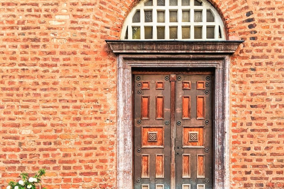 Wooden door with two slabs and reddish-brown panels. The transom window is covered with white wooden grilles. The door is set against a red brick wall