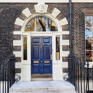 A classic navy blue Georgian front door in London, featuring white stucco rusticated trim, a brass knocker, and a semicircular glass fanlight.