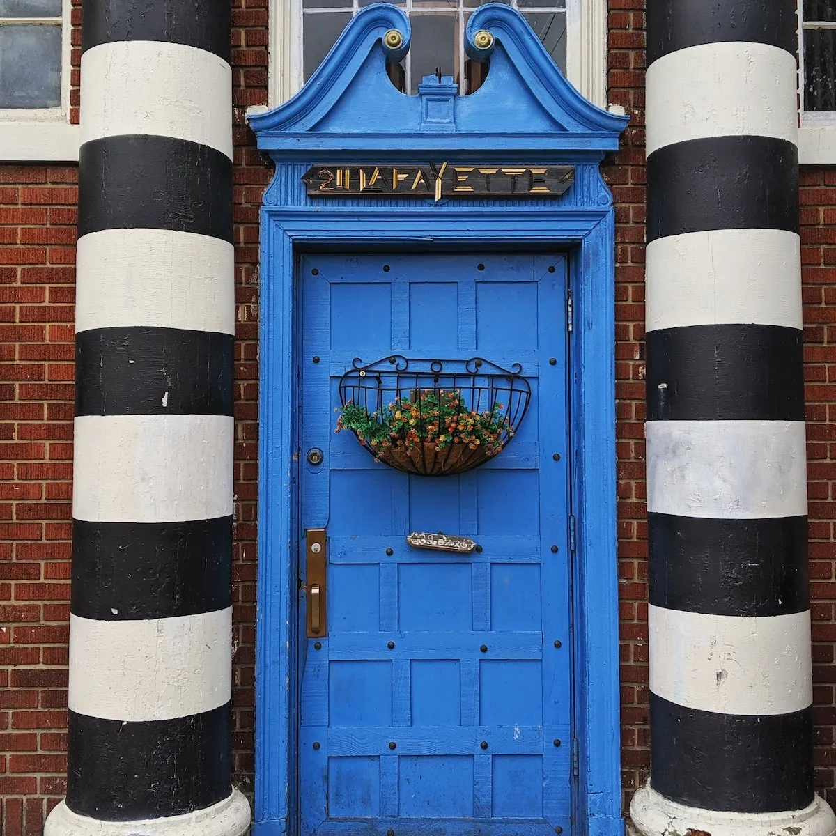 Vibrant blue wooden door with a hanging flower basket, framed by bold black and white striped columns in Buffalo, New York.