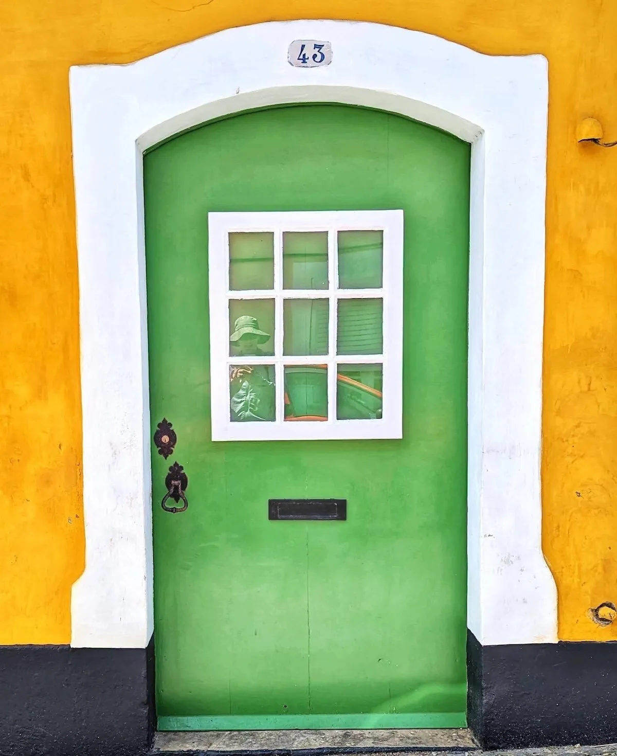 Bright green door numbered 43 with a white nine-pane window and black iron knocker, set against a mustard-yellow wall in Terceira, Azores.