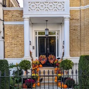 Grand white London townhouse entryway with a black front door, flanked by stone steps lined with autumn leaves and colorful pumpkins.